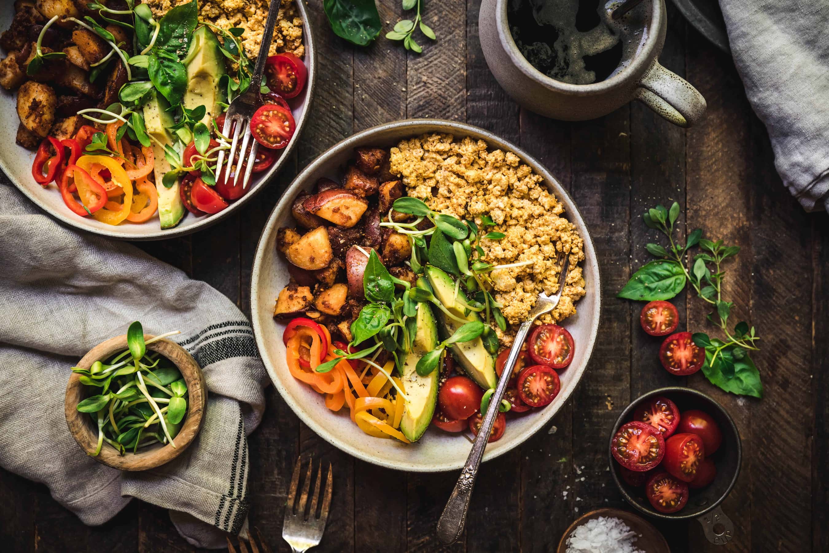 Overhead of two vegan breakfast bowls on a grey background with tomatoes on the side