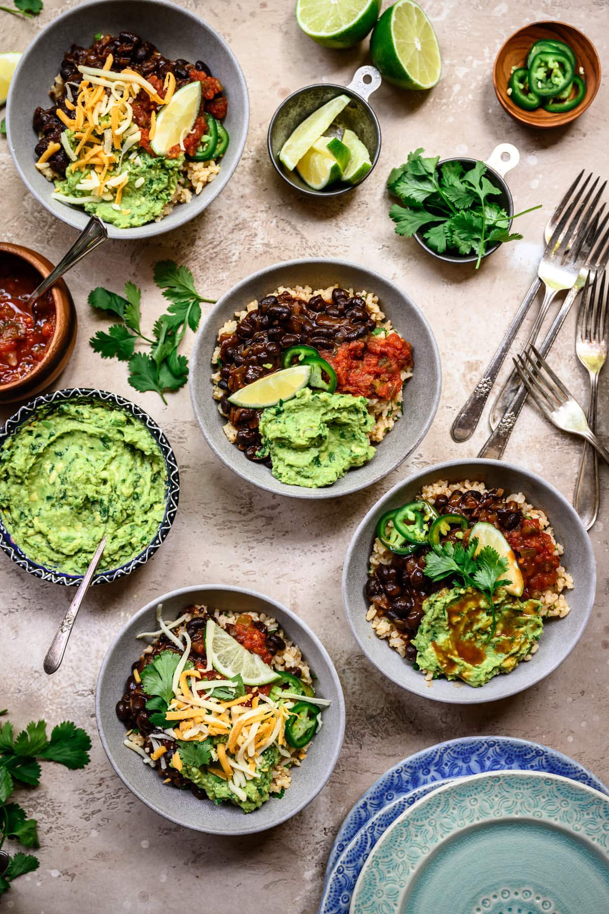 Overhead view of vegan burrito bowls with spicy black beans and guacamole in grey bowls on rustic background