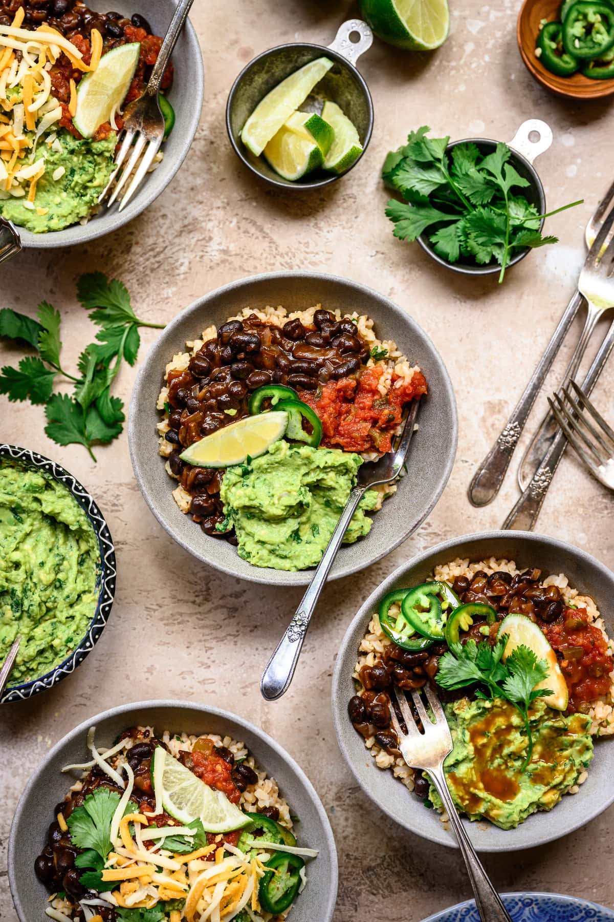 Overhead view of vegan burrito bowls with spicy black beans and guacamole in grey bowls on rustic background