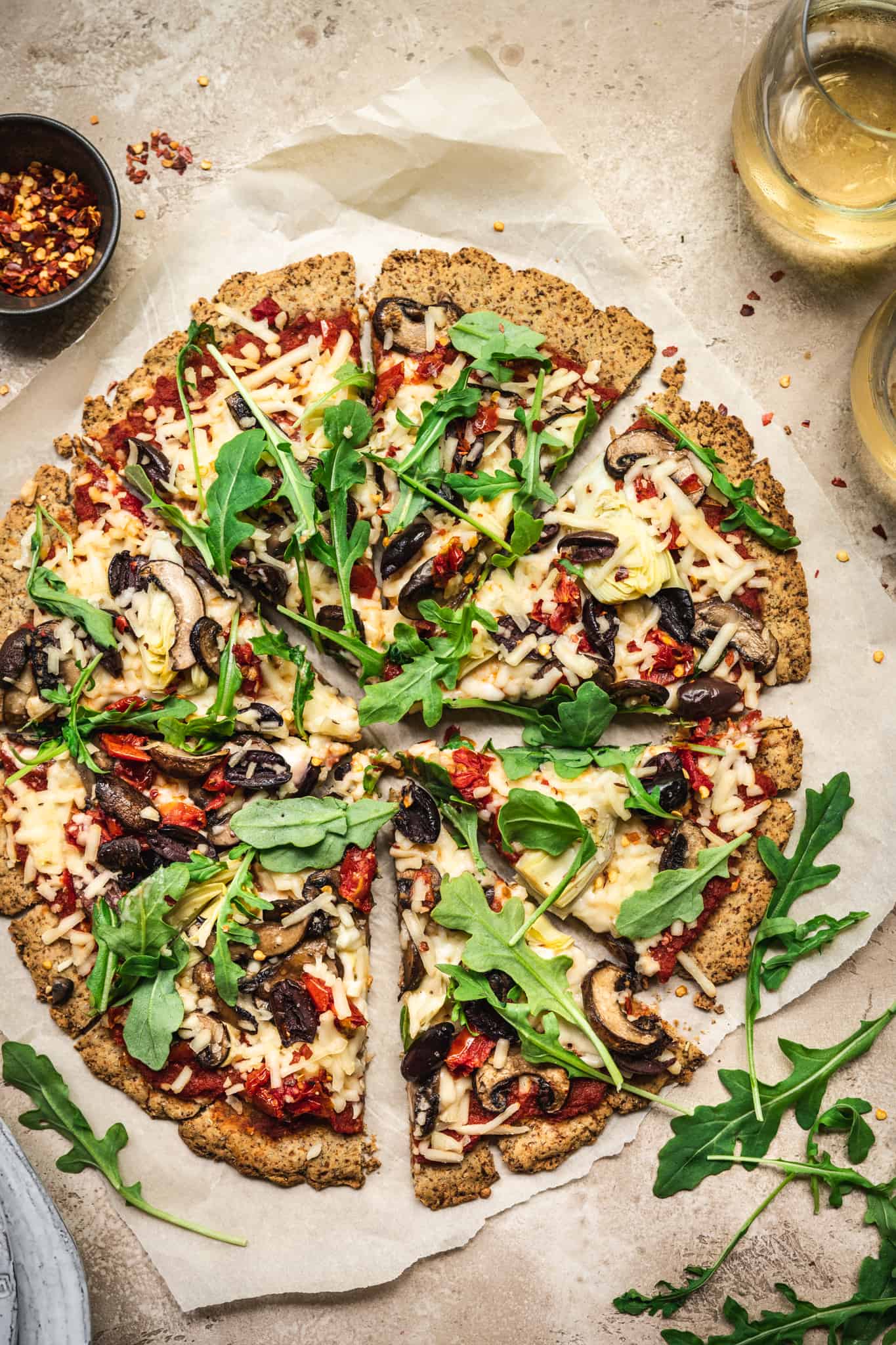 Overhead view of Crispy Cauliflower Vegan Pizza Crust with vegan pizza toppings on rustic background with white wine
