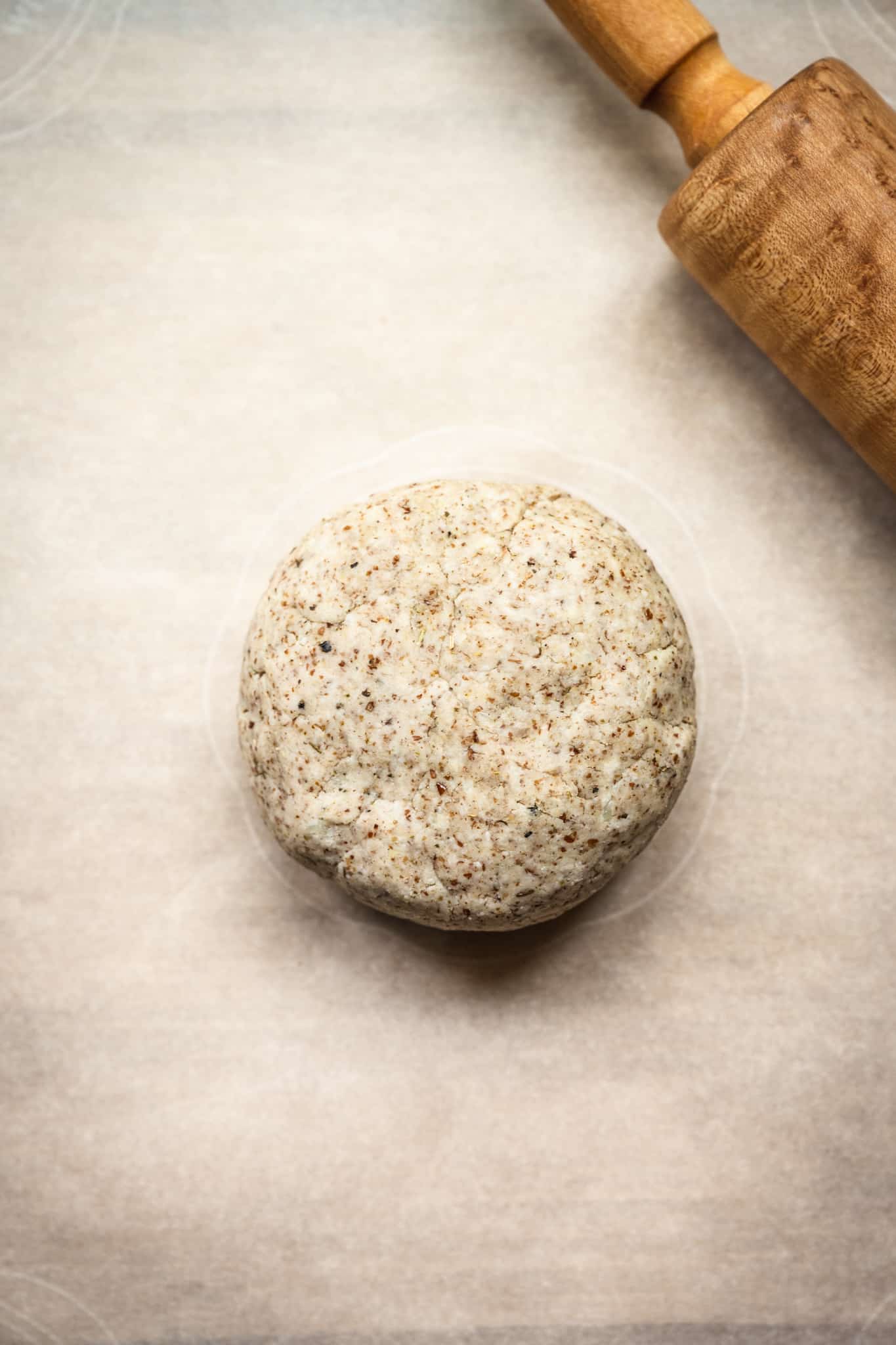 Overhead of ball of vegan cauliflower crust dough on parchment paper next to rolling pin