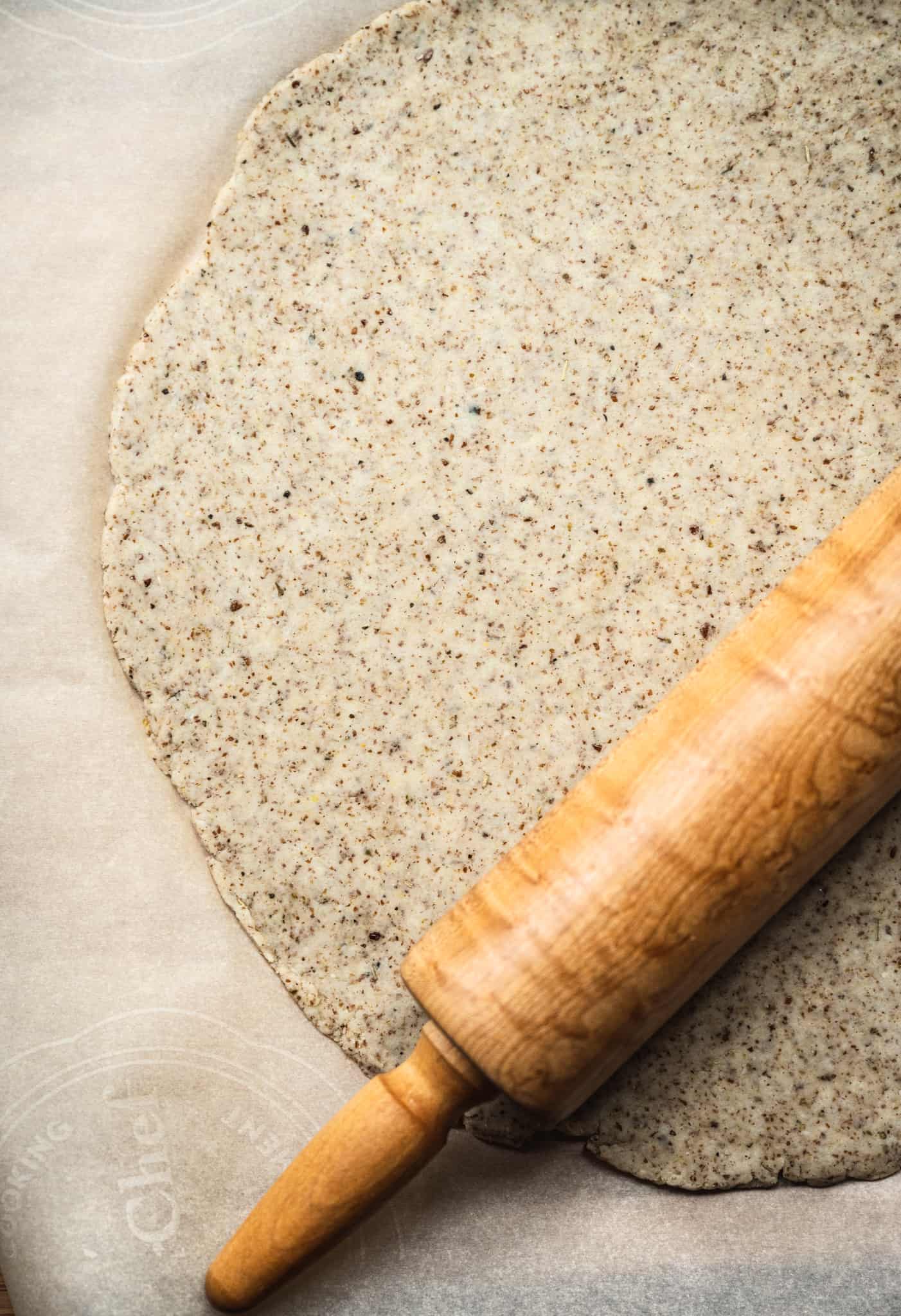 Overhead view of pizza crust being rolled out with rolling pin on parchment paper