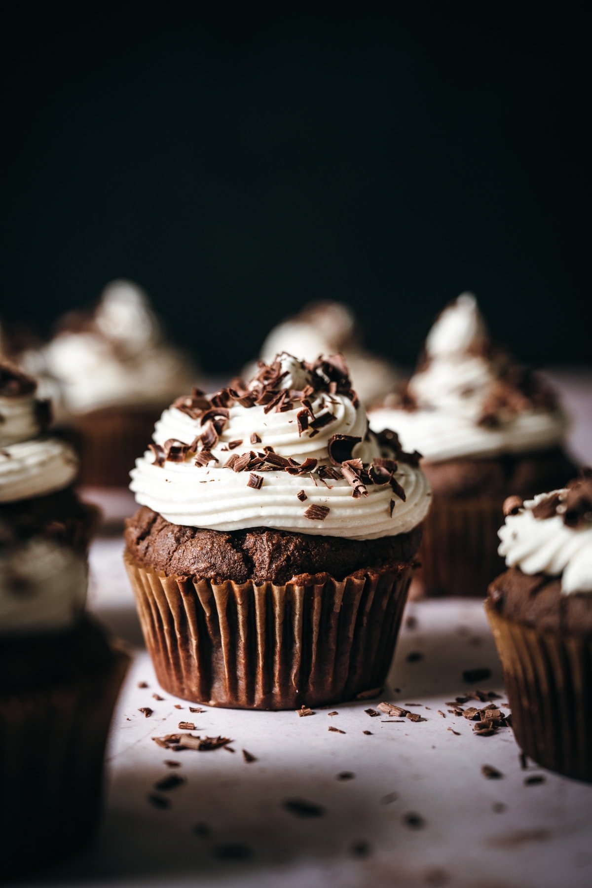 close up side view of vegan chocolate cupcake topped with vanilla frosting and chocolate shavings. 