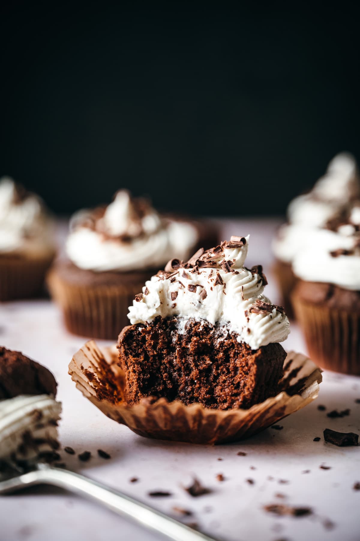 side view of vegan chocolate cupcake topped with vanilla frosting with bite taken out. 