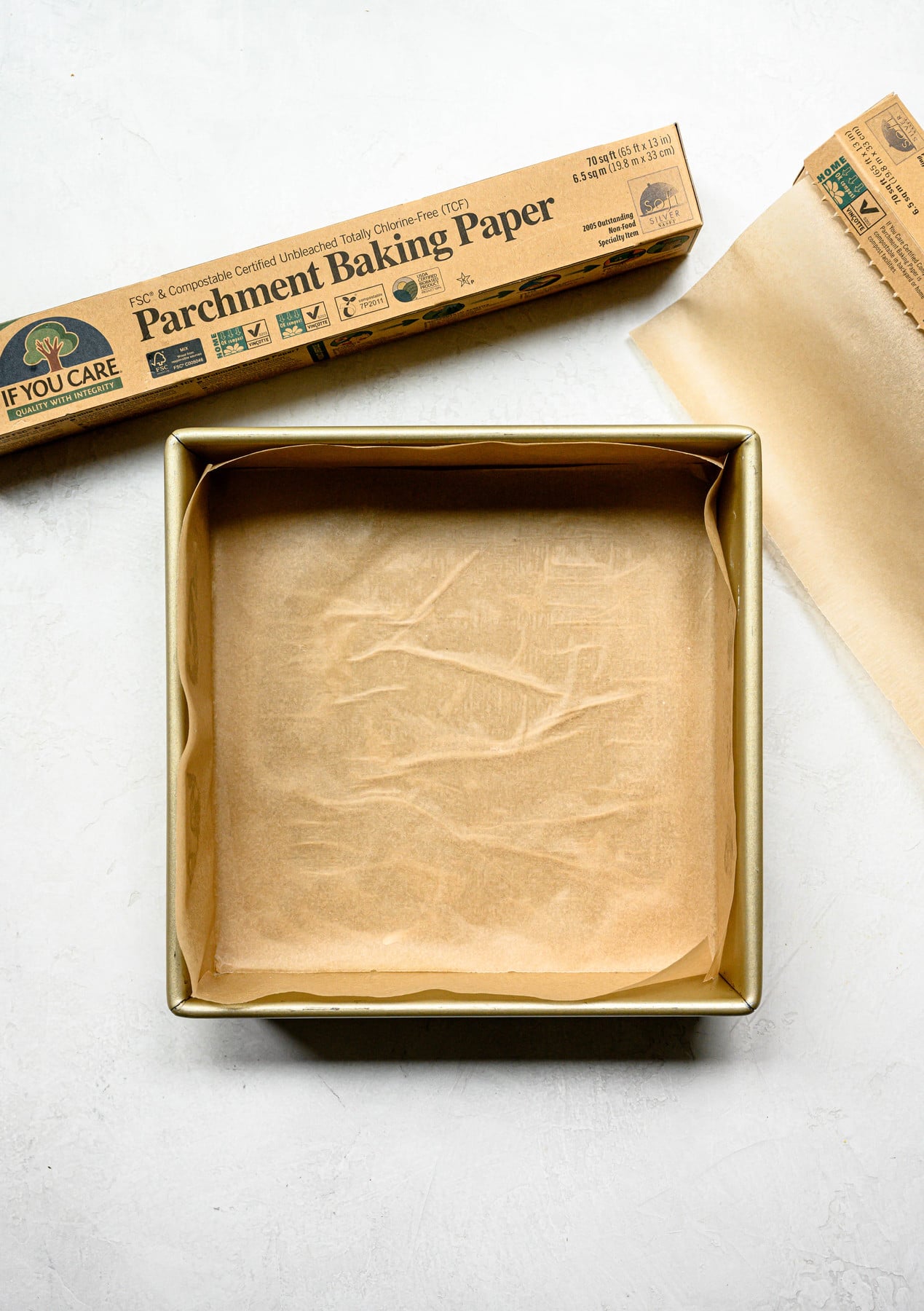 Overhead view of parchment paper in square brownie pan on white background