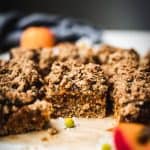 side view of apricot oat bars on parchment paper with fresh apricots in background