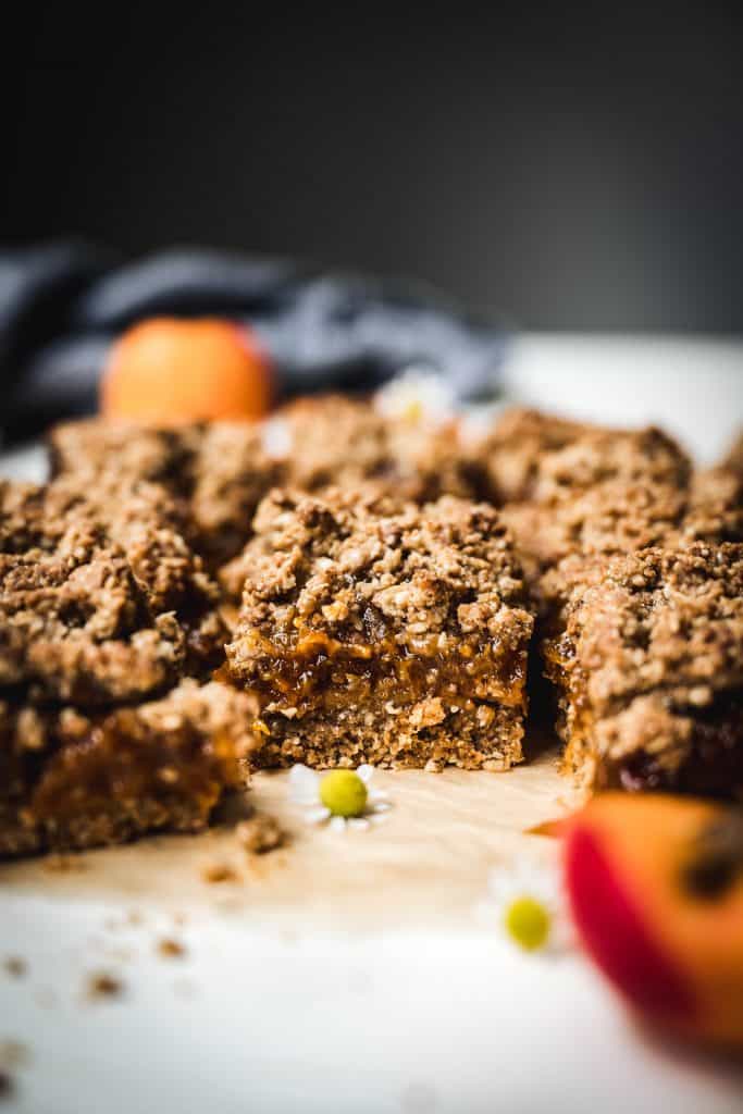 side view of apricot oat bars on parchment paper with fresh apricots in background