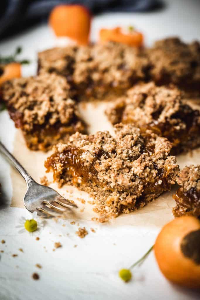 side view of apricot oat bar with fork next to it on white surface