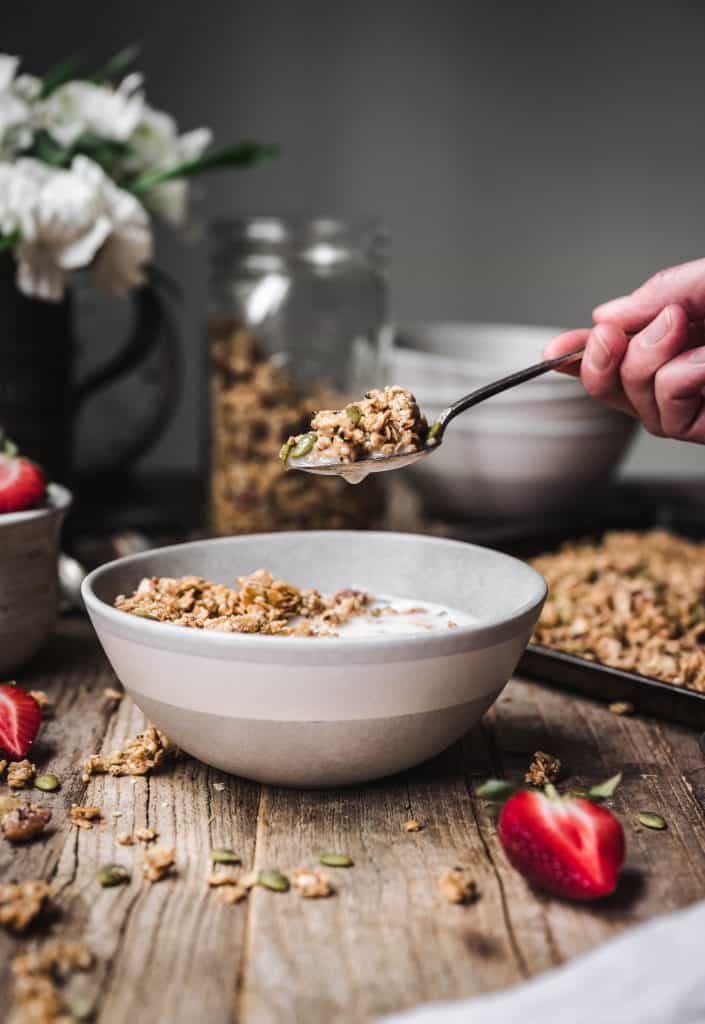 Person holding spoon of granola over bowl