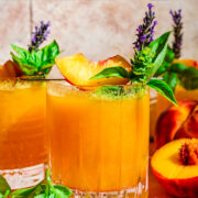 Close up view of peach bourbon smash in glass with basil and peach garnish.