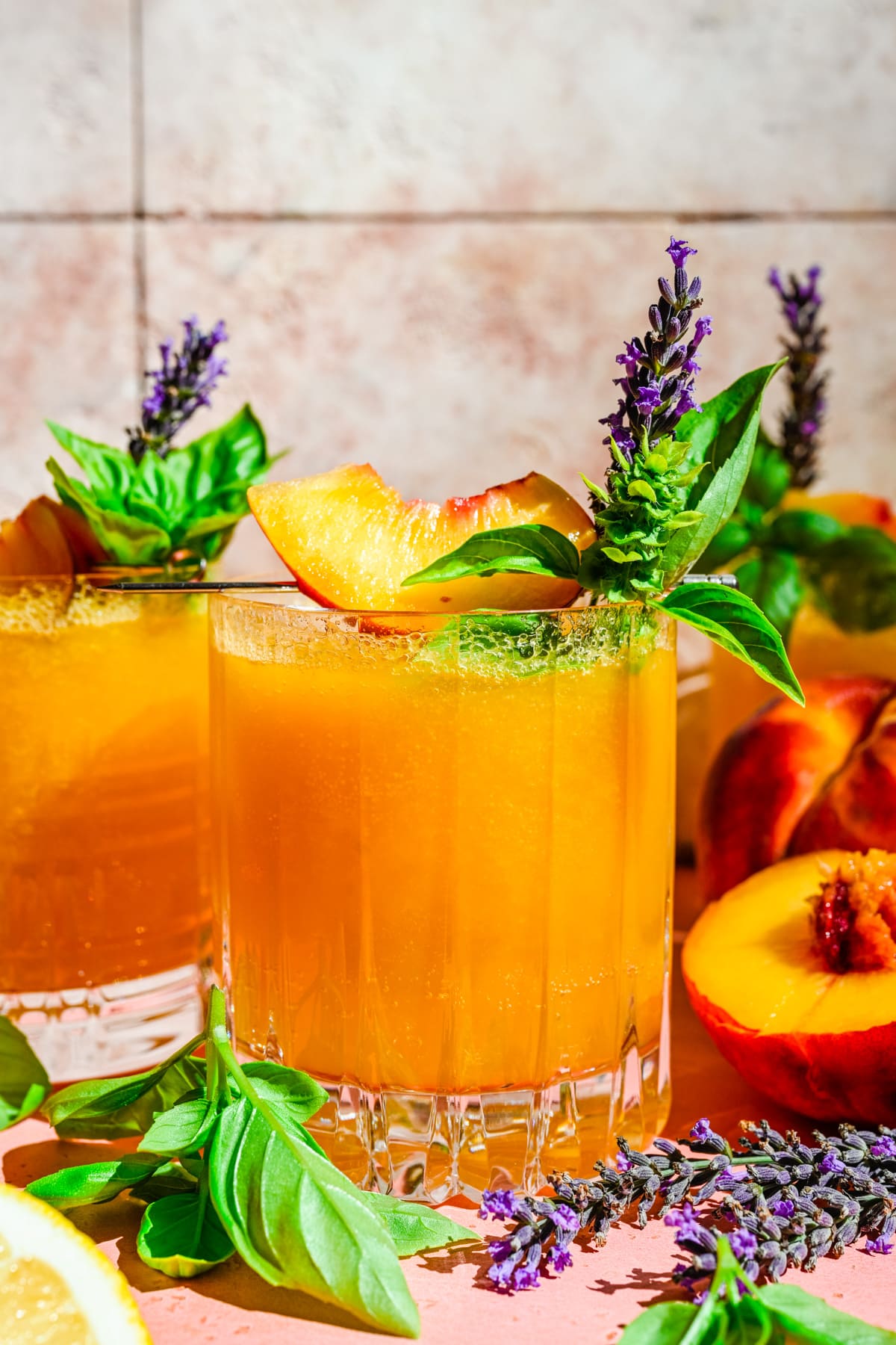 Close up view of peach bourbon smash in glass with basil and peach garnish. 
