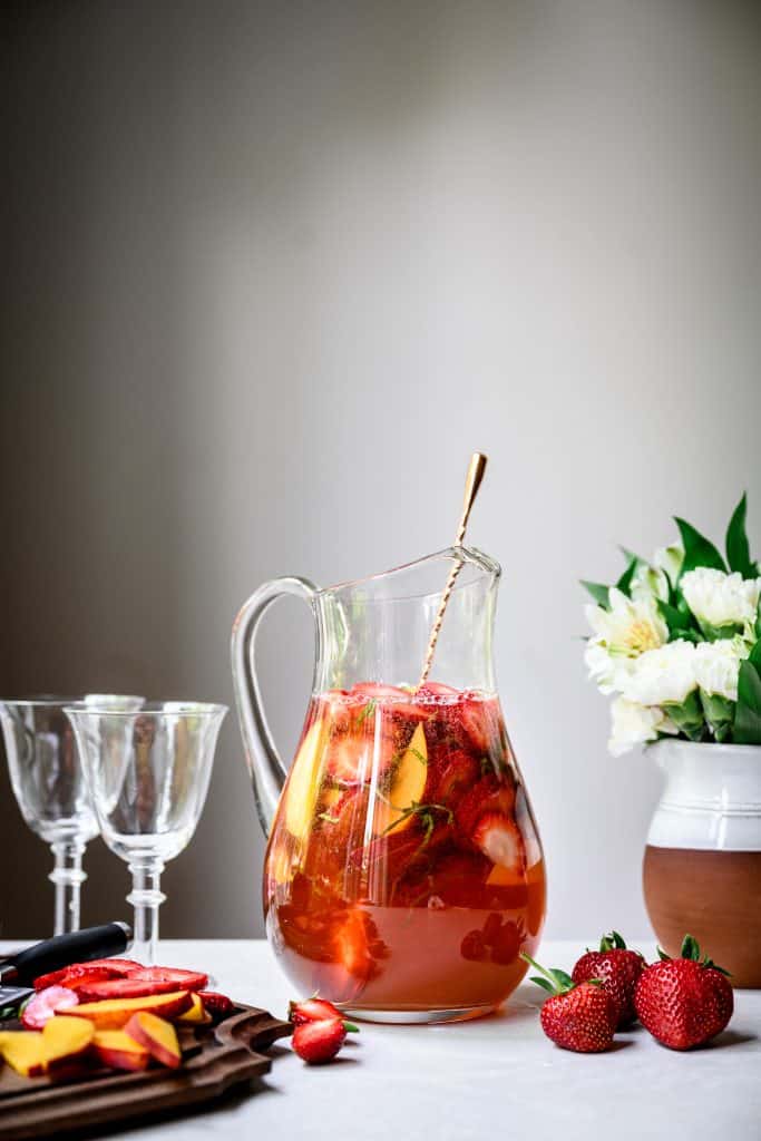side view of strawberry peach basil white wine sangria on white background