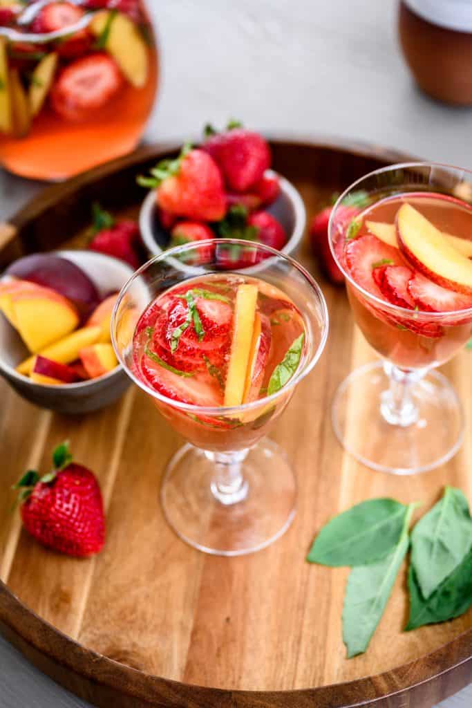 Side view of strawberry peach sangria in a cocktail glass on wood tray
