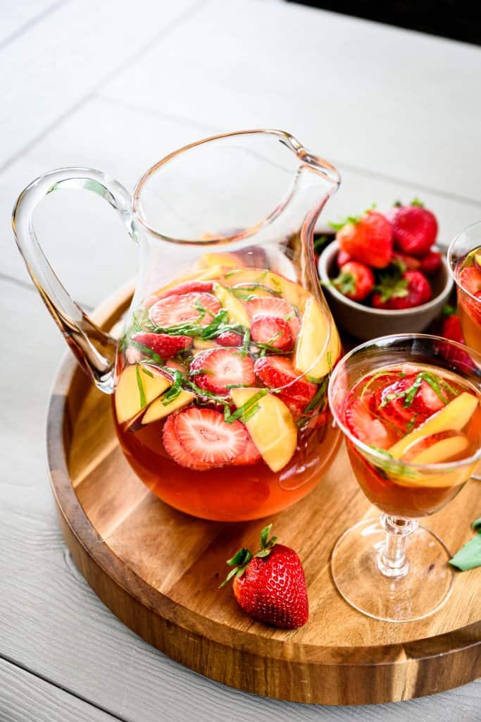 Side view of strawberry peach basil sangria in a large pitcher on wood tray