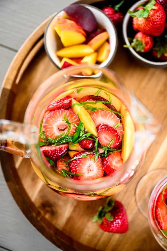 close up overhead of strawberry peach basil white wine sangria in a large pitcher