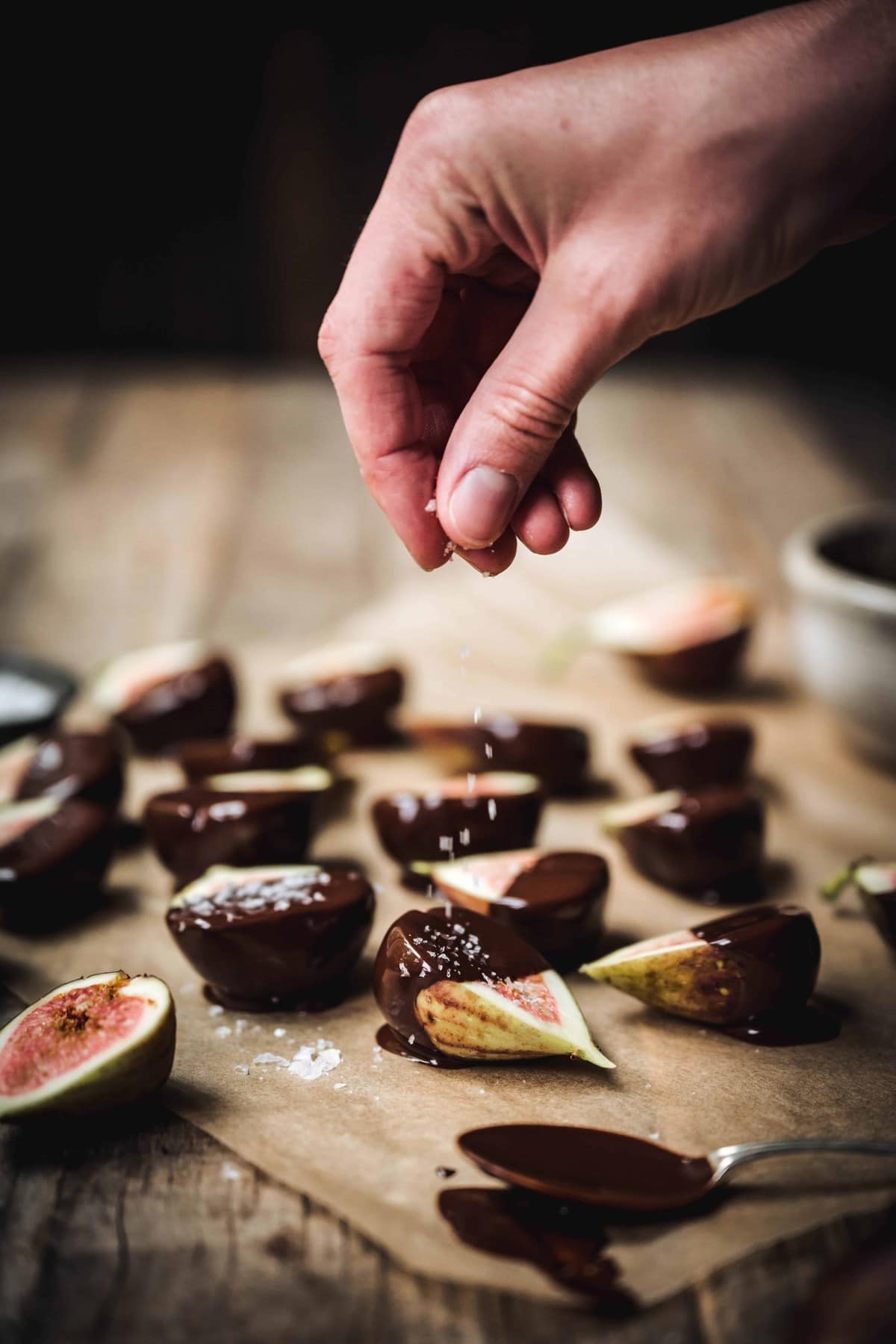 Person sprinkling flaky salt on chocolate dipped figs