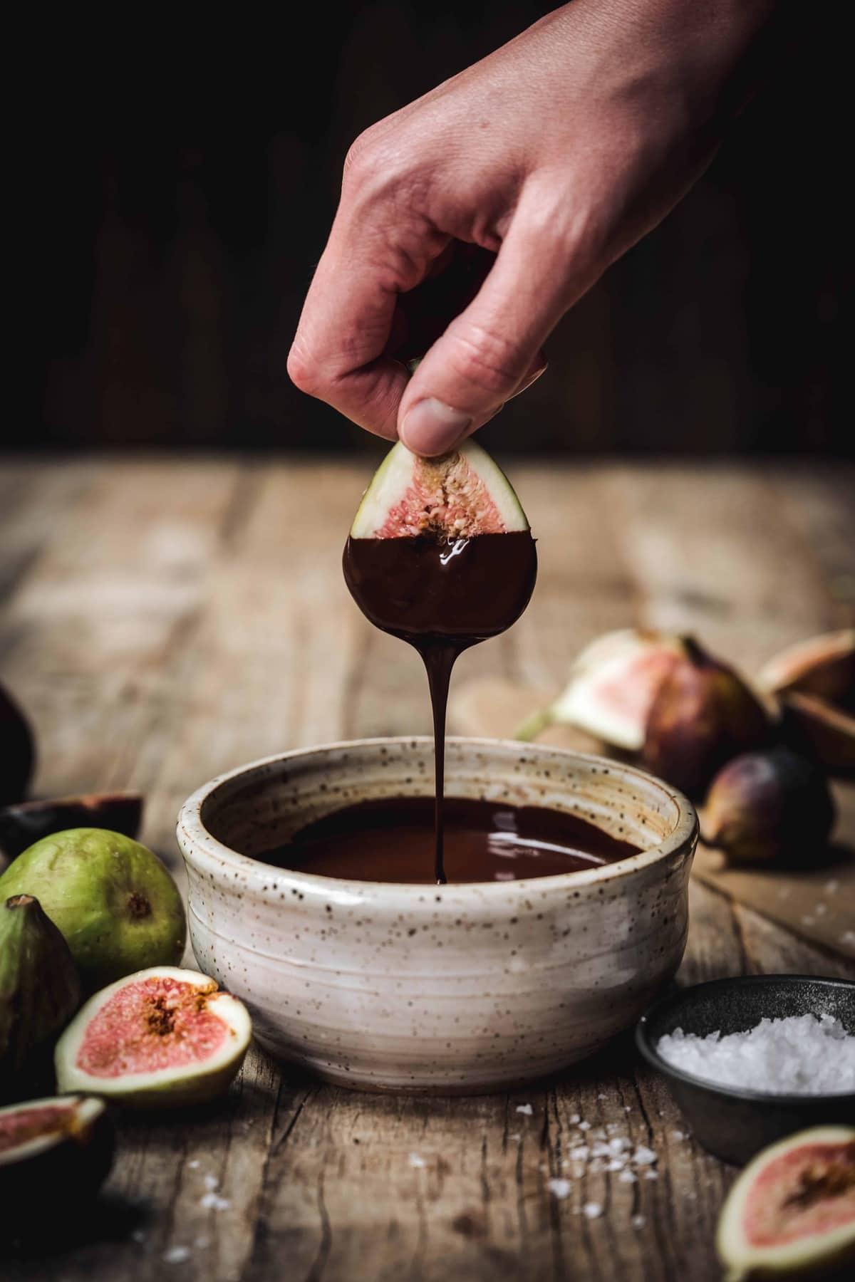 person dipping fresh fig in melted dark chocolate