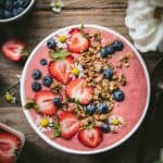 Overhead view of beautiful strawberries and cream smoothie bowl with fresh berries and granola on wood table