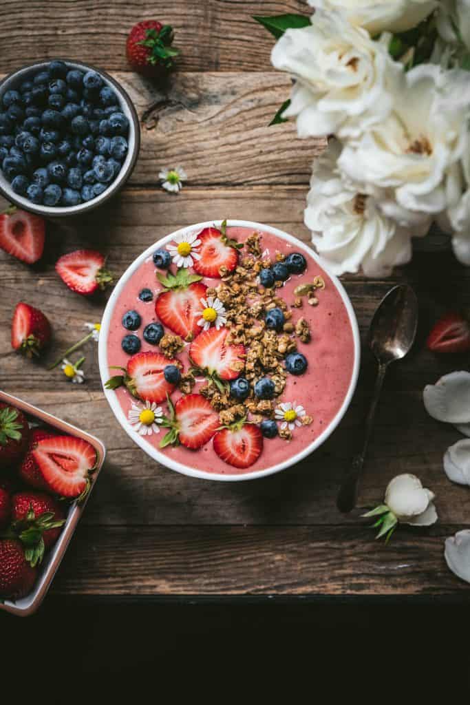 Overhead view of beautiful strawberries and cream smoothie bowl with fresh berries and granola on wood table