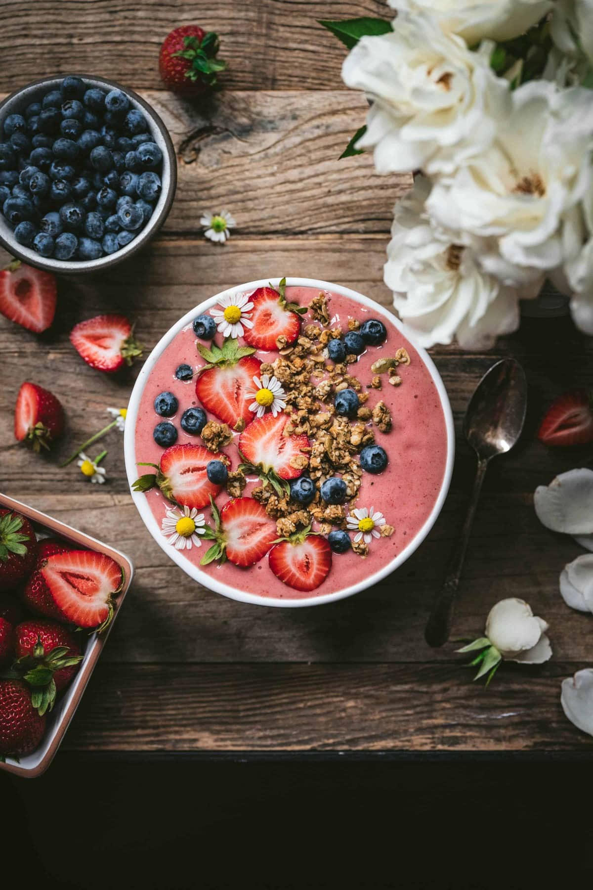 Overhead view of strawberries and cream smoothie bowl with fresh berries and granola on wood table