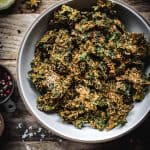 Close up of cheesy vegan kale chips in a white bowl on wood table