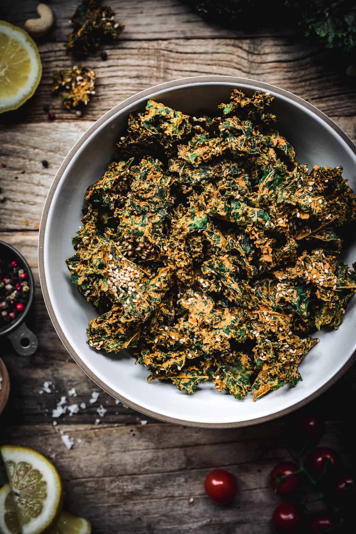 Close up of cheesy vegan kale chips in a white bowl on wood table