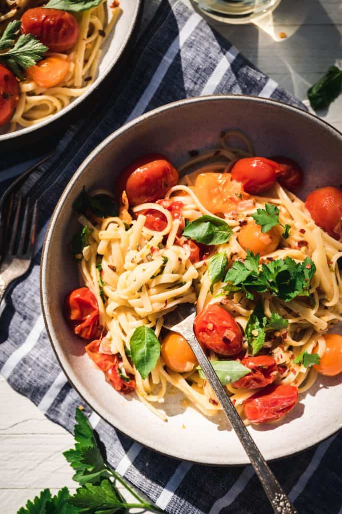 Close up Overhead view of simple burst cherry tomato pasta in a bowl in direct sunlight with glass of white wine