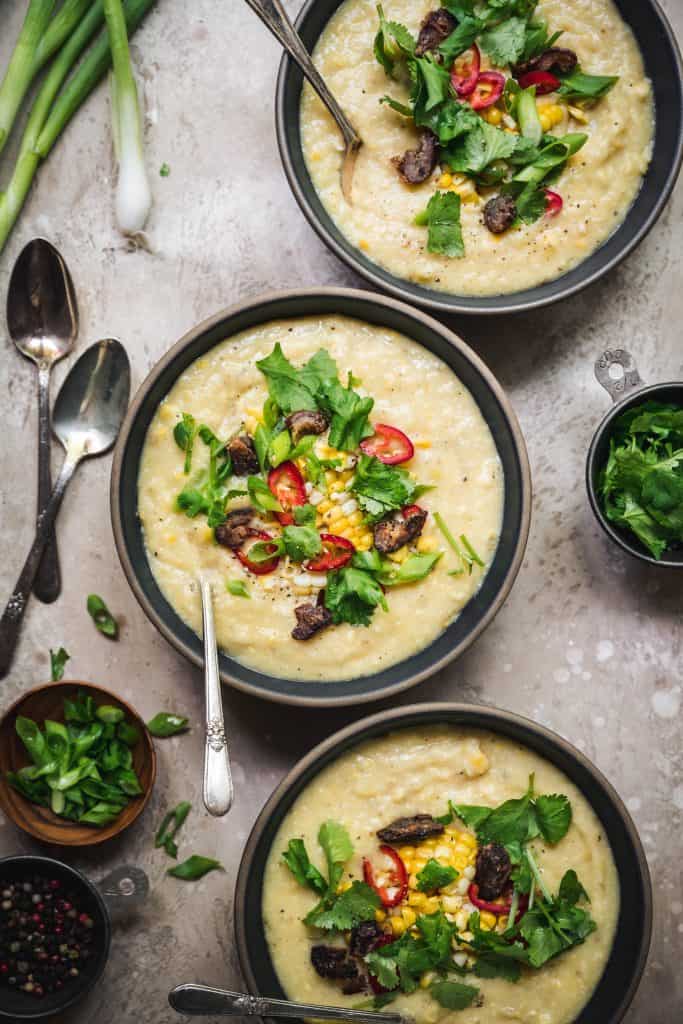 overhead of three bowls of vegan coconut corn chowder with crispy dates and fresh herbs