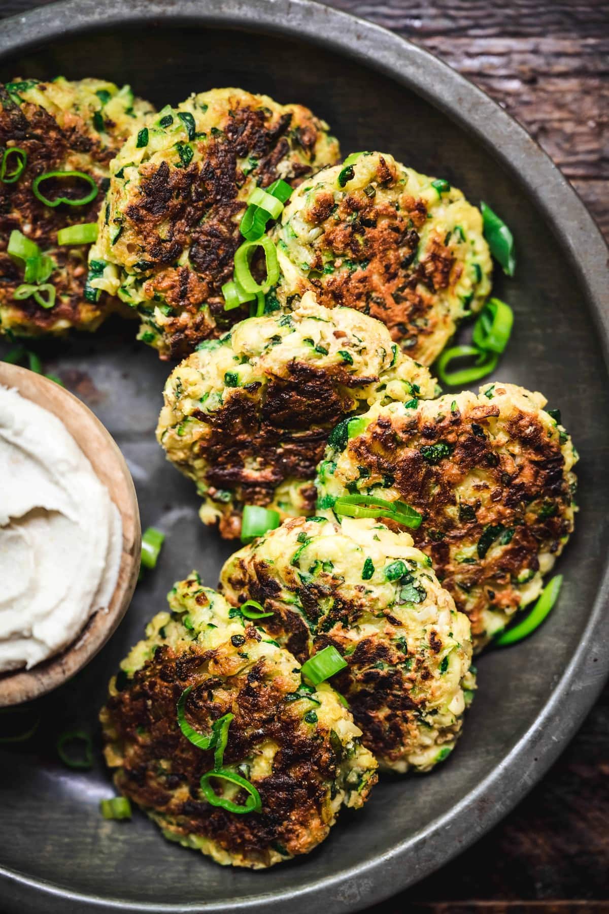 overhead of vegan pesto zucchini fritters on a metal dish with dairy free lemon cashew cream sauce