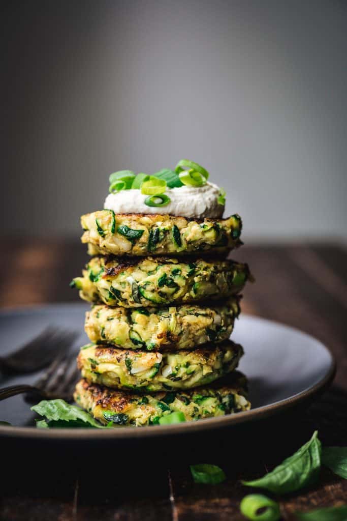 side view of a stack of gluten free zucchini fritters with vegan lemon cashew cream on top