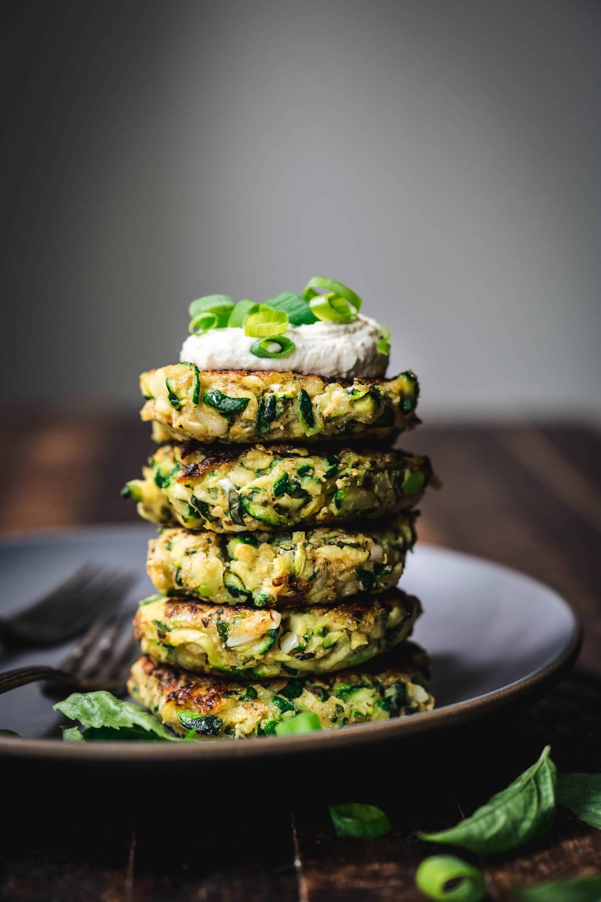 side view of a stack of gluten free zucchini fritters with vegan lemon cashew cream on top