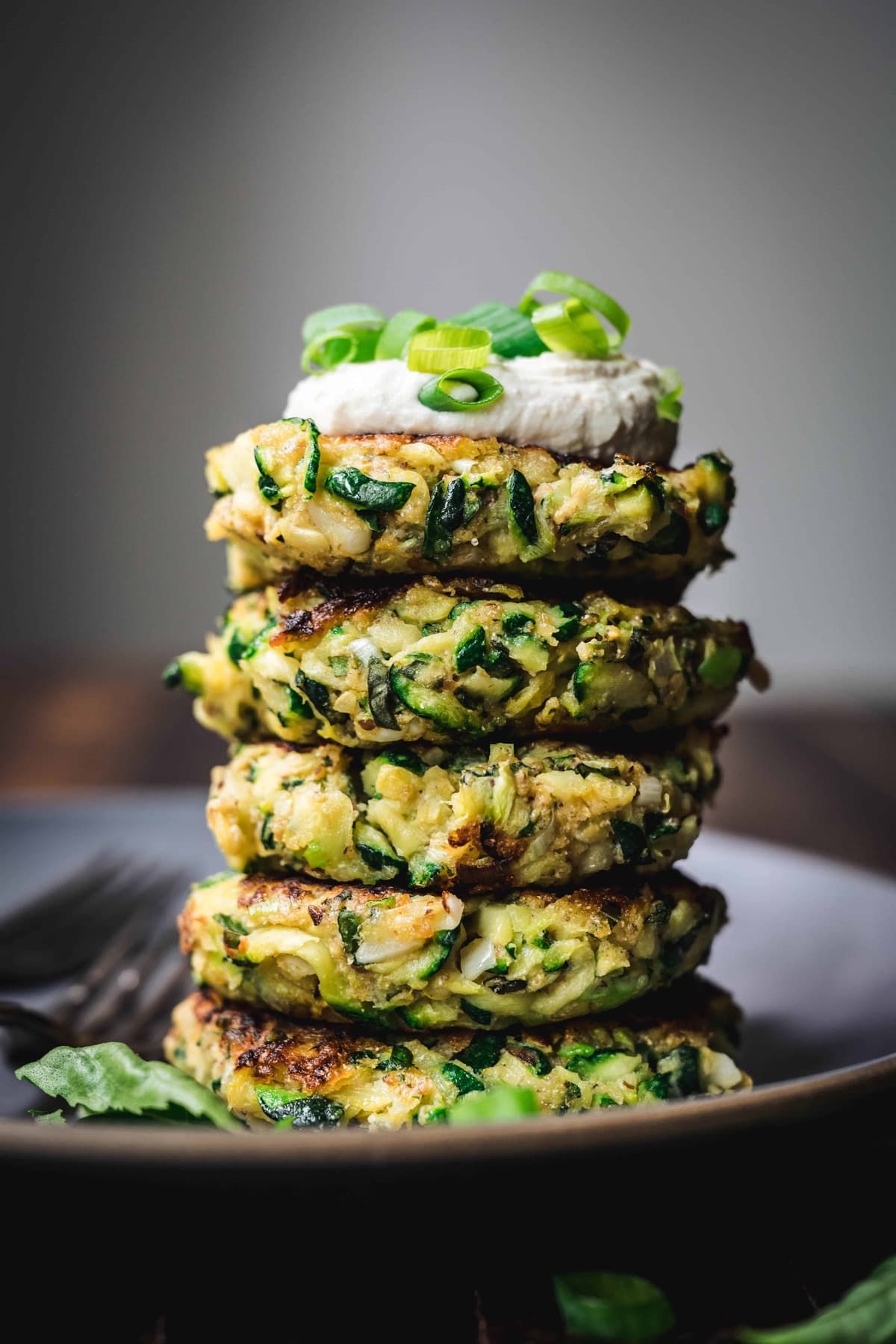 side view of a stack of gluten free zucchini fritters with lemon cashew cream and scallions