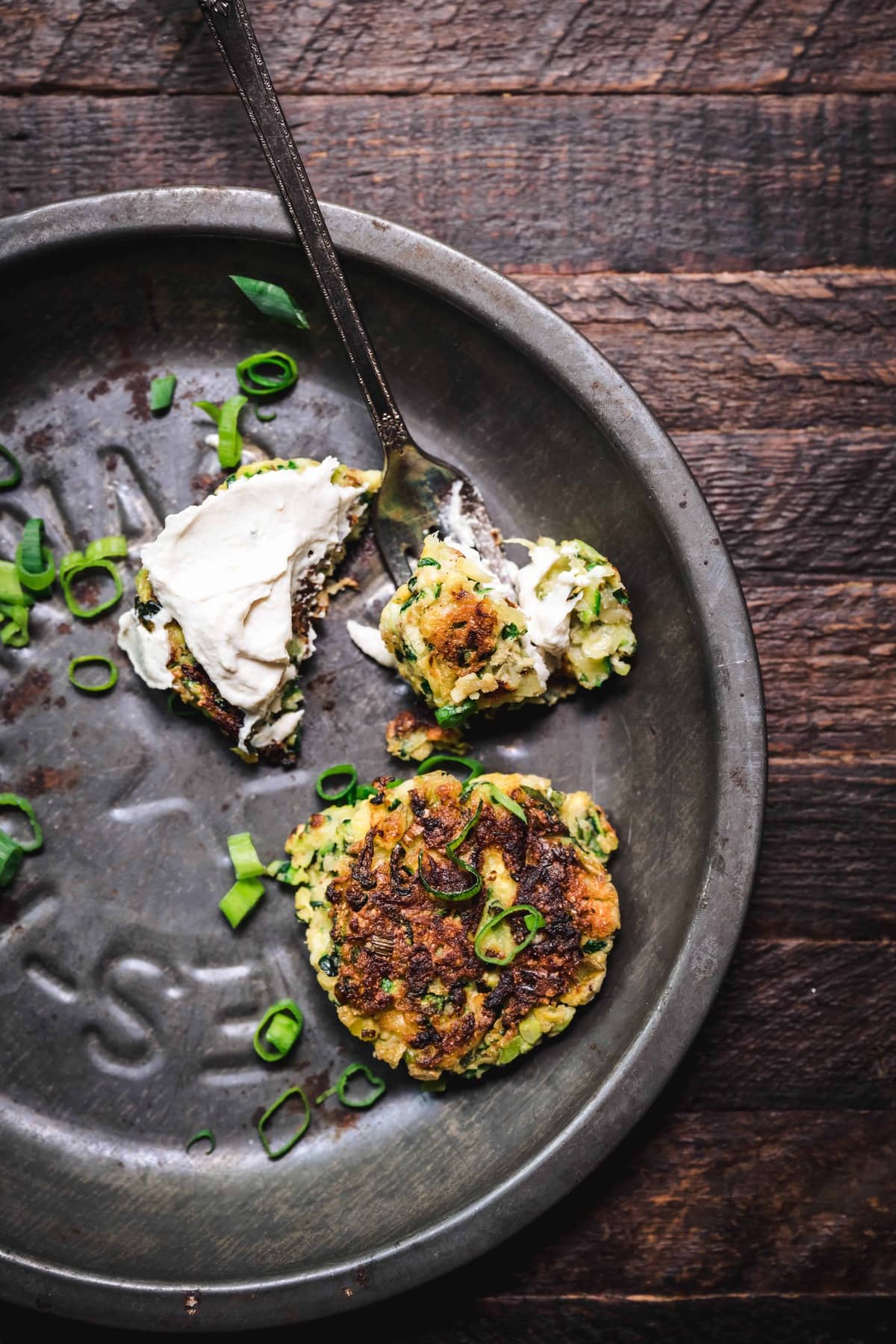 overhead of a vegan and gluten free zucchini fritter on a pan that's been eaten with a fork