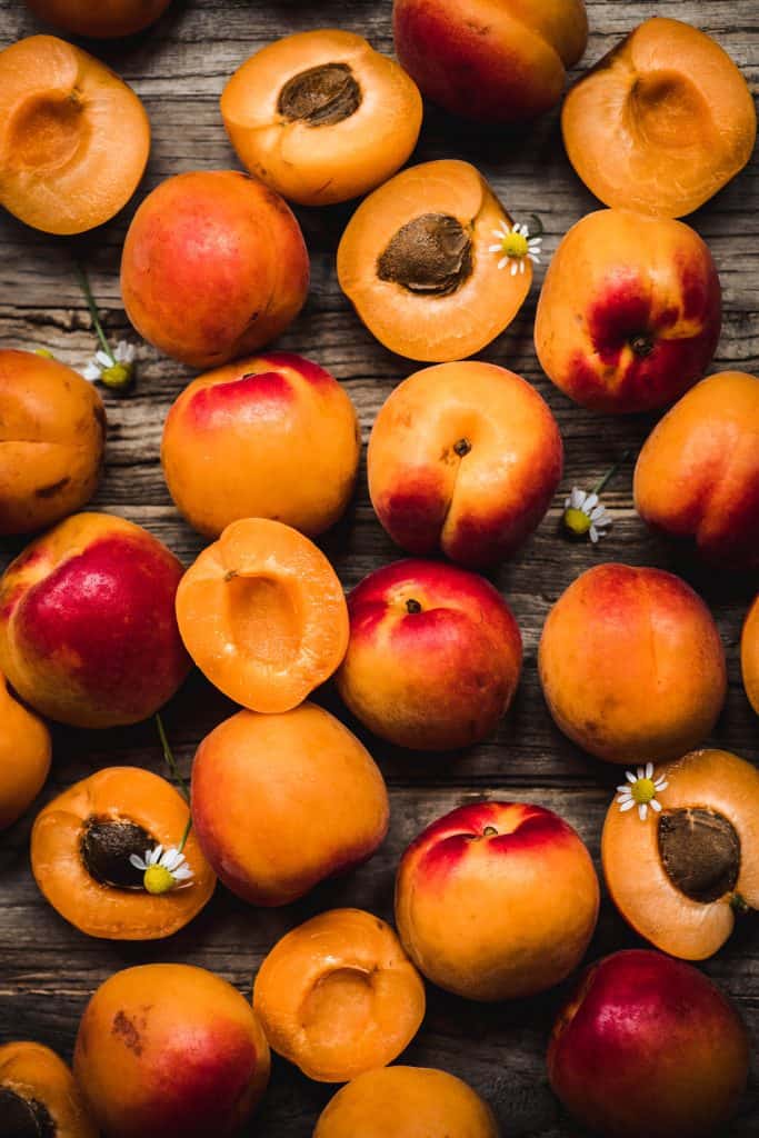 overhead view of beautiful fresh apricots with chamomile flowers on rustic wood background