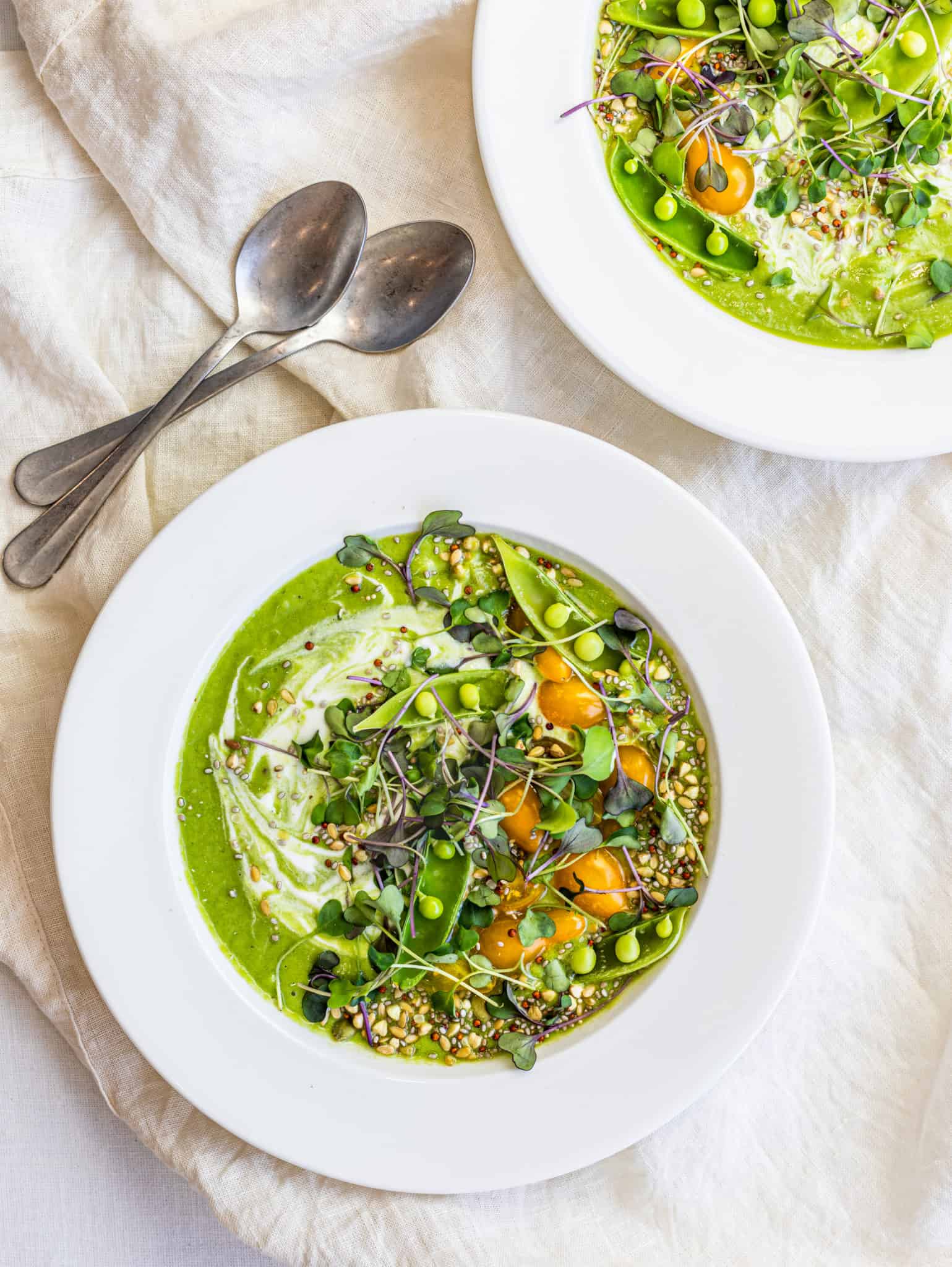 overhead of two bolws of chilled vegan cucumber avocado soup with toppings