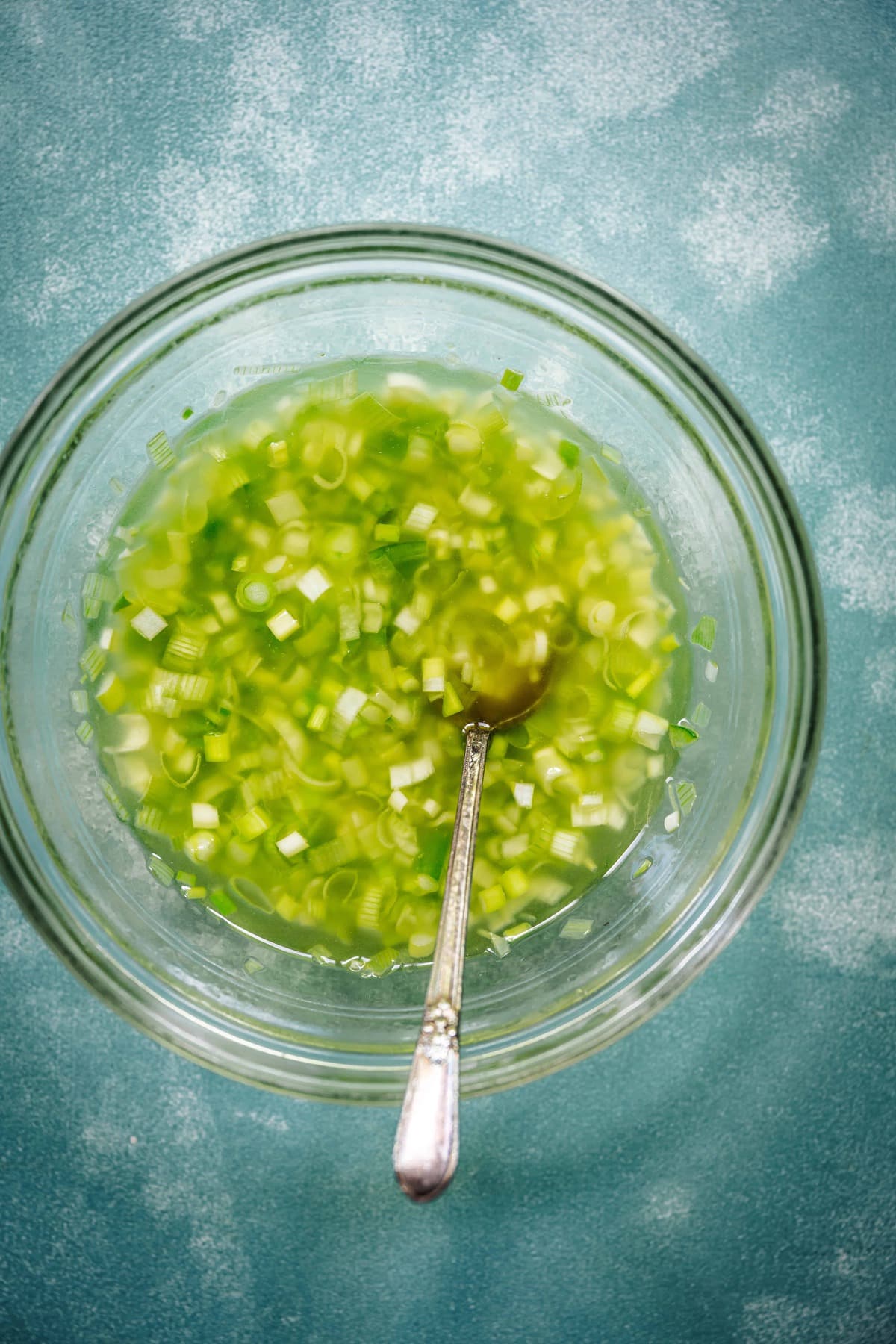 overhead of citrus scallion dressing in a bowl with a silver spoon