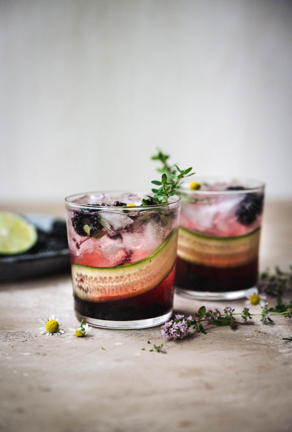 side view of two blackberry cucumber gin cocktails with fresh herb garnish