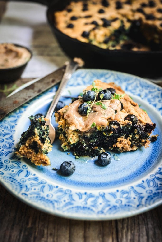 side view of a slice of vegan blueberry cornbread with honey thyme butter on a blue plate with a bite taken out