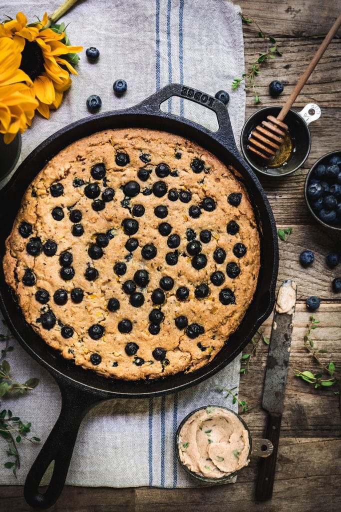 overhead of vegan blueberry cornbread in a skillet with homemade vegan honey thyme butter on the side
