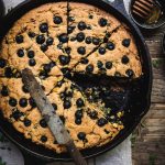 overhead of gluten free blueberry cornbread in a cast iron skillet with a slice removed