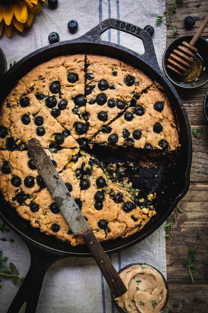 overhead of gluten free blueberry cornbread in a cast iron skillet with a slice removed