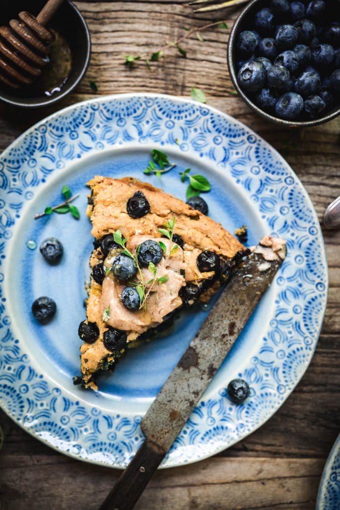overhead of a slice of gluten free blueberry cornbread on a blue plate with a butter knife