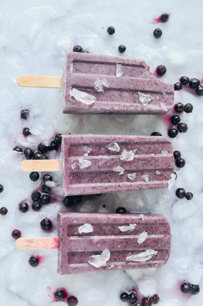 overhead of vegan blueberry basil popsicles on a white background
