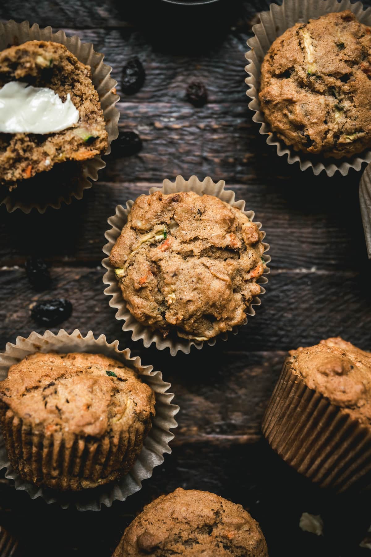 overhead of several gluten free vegan carrot zucchini muffins in liners on a dark wood background