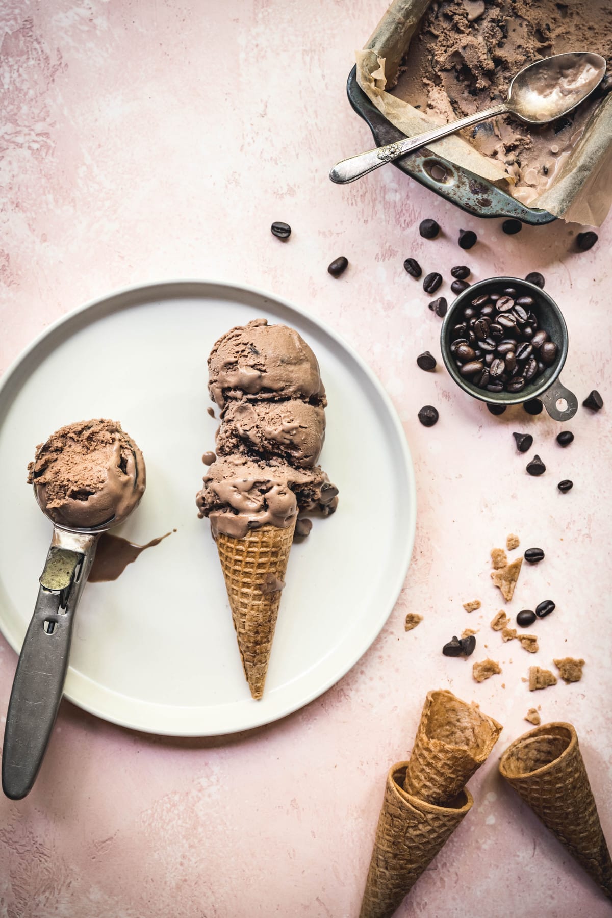 overhead of three scoops of vegan mocha ice cream in a cone on a white plate