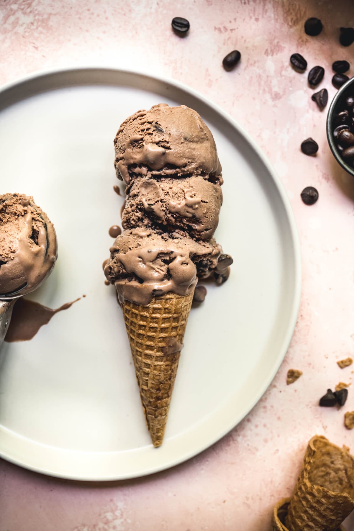 overhead of three scoops of vegan mocha ice cream in a cone on a white plate