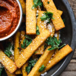 overhead of vegan polenta fries in a round dish with homemade marinara sauce
