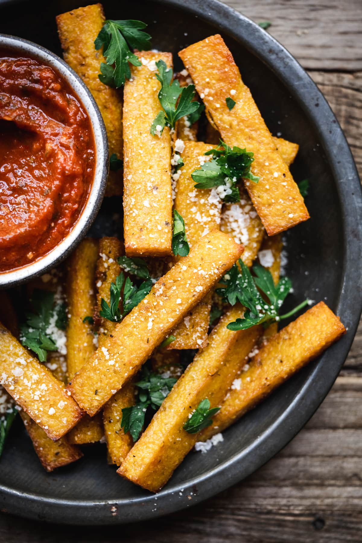 overhead of vegan polenta fries in a round dish with homemade marinara sauce