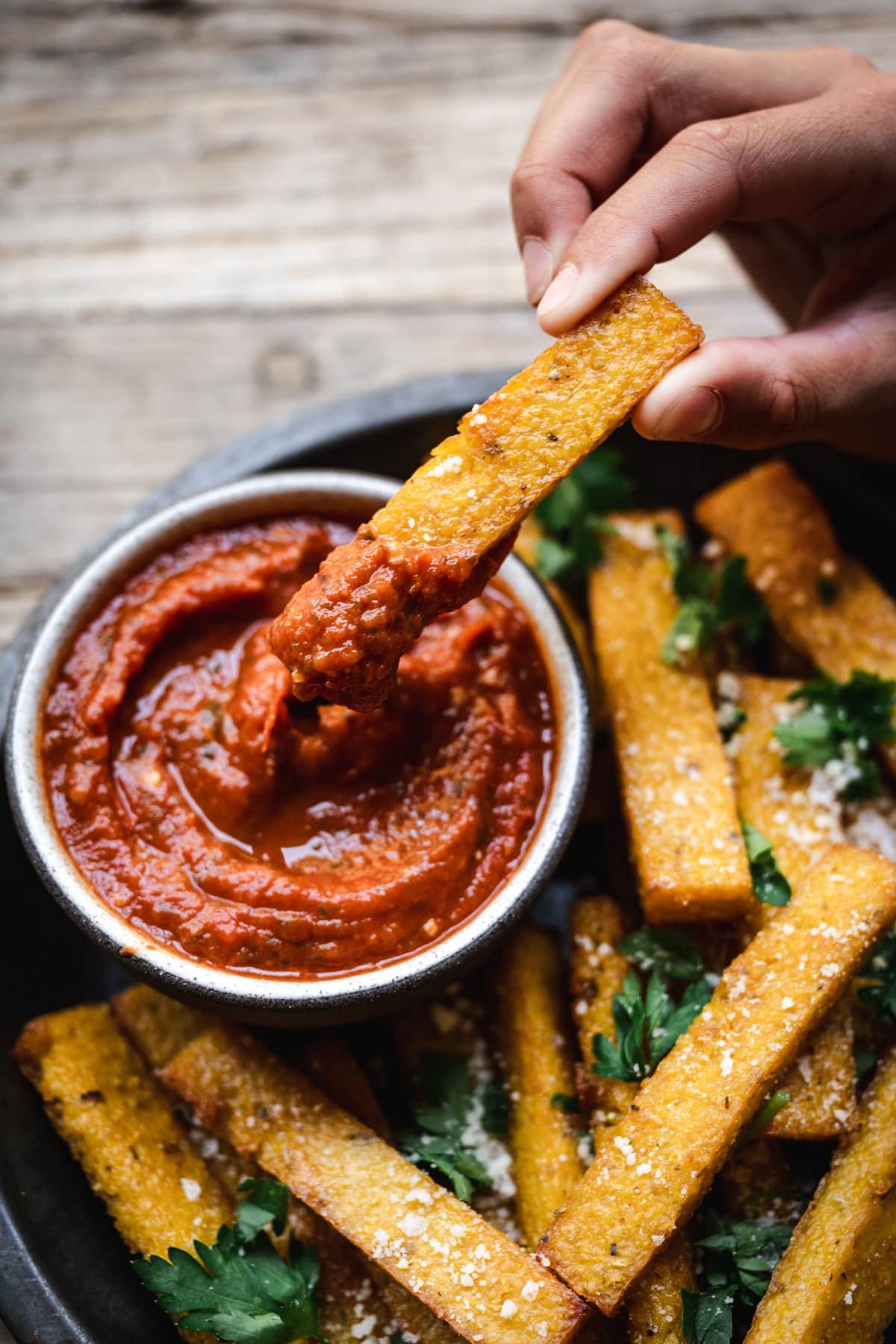 overhead of a person dipping crispy vegan polenta fries in homemade marinara sauce