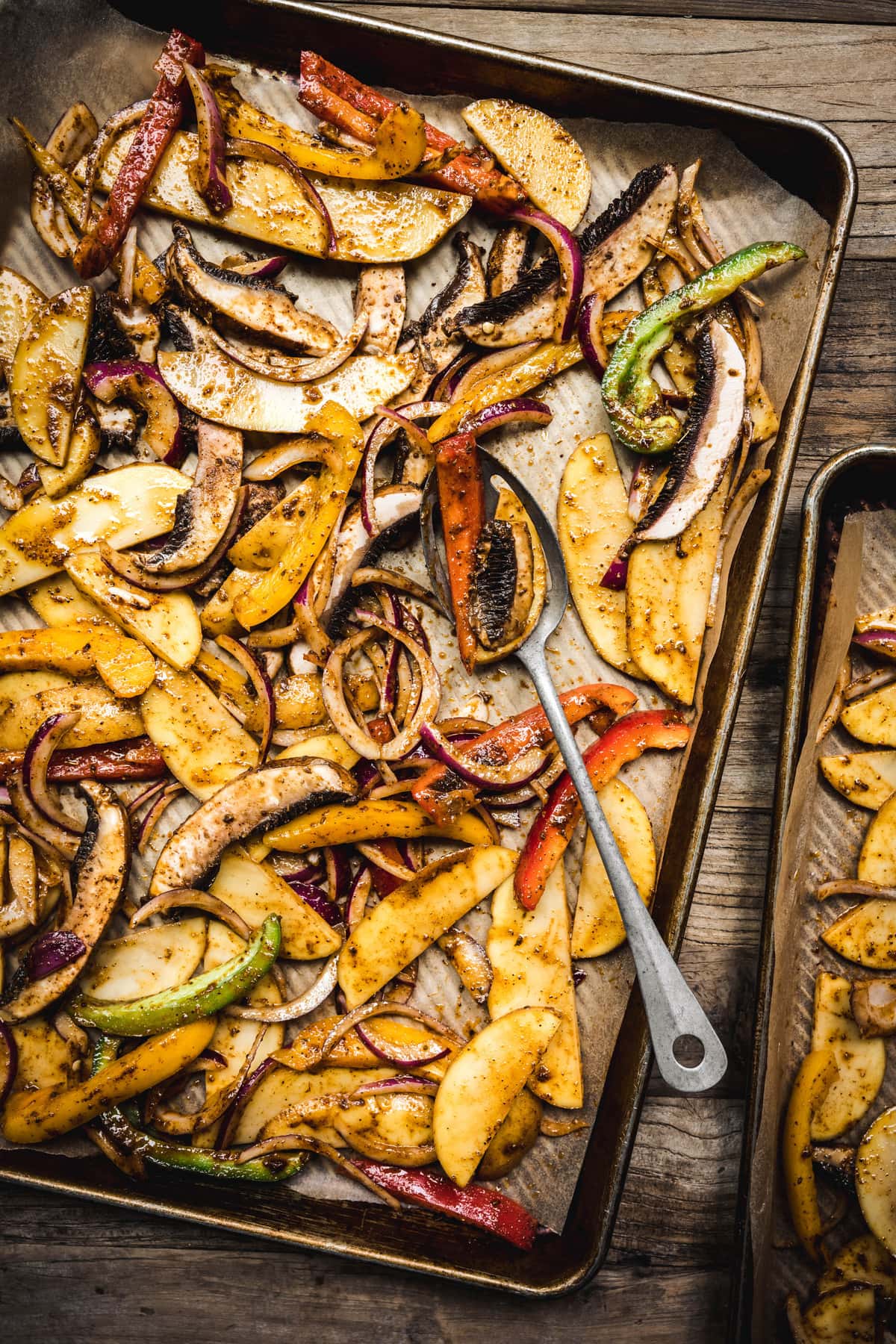 overhead of potatoes, peppers, onions and mushrooms with fajita seasoning on a sheet pan